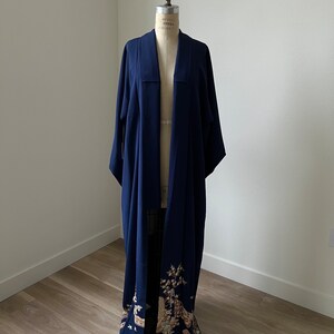 Könnte beinhalten: Ein marineblauer Kimono mit einem floralen Muster am unteren Saum. Der Kimono wird auf einer Schaufensterpuppe präsentiert.