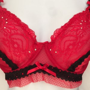 May include: Red lace bra with black trim and rhinestones. The bra has a bow in the center and a scalloped edge.