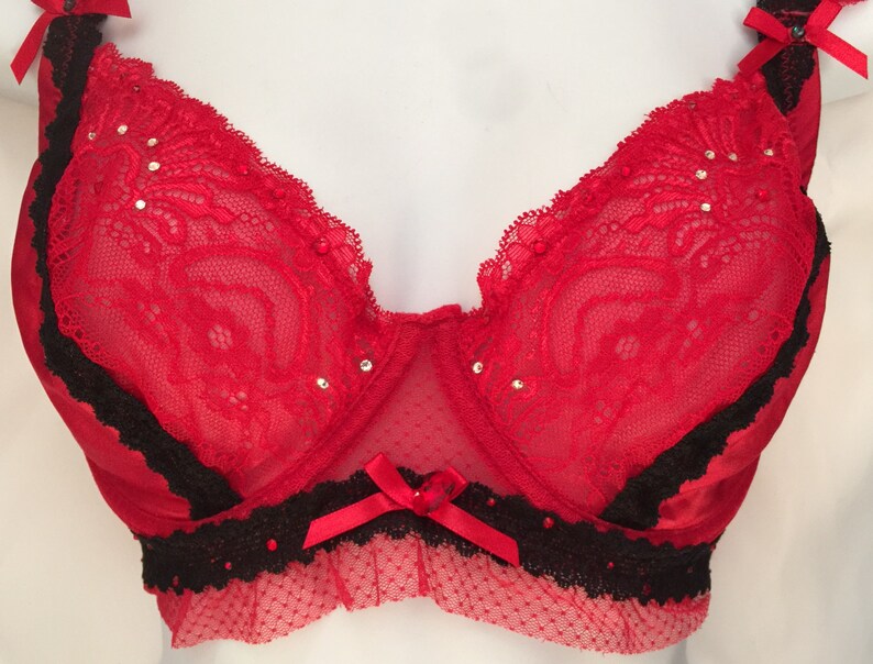 May include: Red lace bra with black trim and rhinestones. The bra has a bow in the center and a scalloped edge.