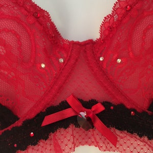 May include: Red lace bra with black trim and a red bow with a heart-shaped embellishment.