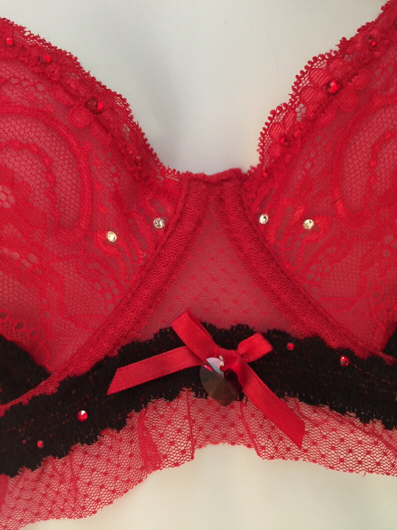 May include: Red lace bra with black trim and a red bow with a heart-shaped embellishment.