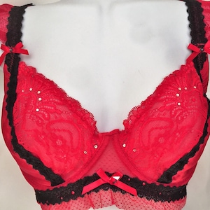 May include: Red lace bra with black trim and bows. The bra has a delicate floral pattern and is adorned with rhinestones.