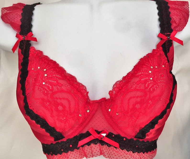 May include: Red lace bra with black trim and bows. The bra has a delicate floral pattern and is adorned with rhinestones.