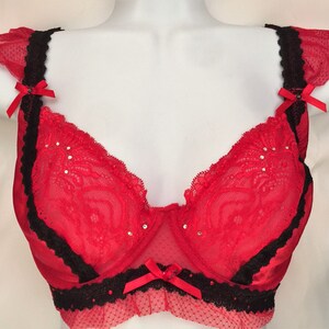 May include: Red lace bra with black trim and a bow on the center. The bra has a sheer mesh fabric and is decorated with rhinestones.