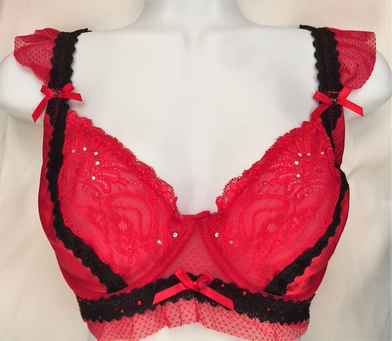 May include: Red lace bra with black trim and a bow on the center. The bra has a sheer mesh fabric and is decorated with rhinestones.