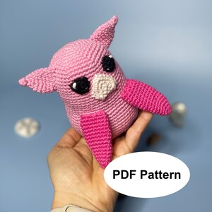 May include: Pink crocheted owl amigurumi toy with black eyes and a white beak. The owl is holding a pink wing in its hand. PDF Pattern.
