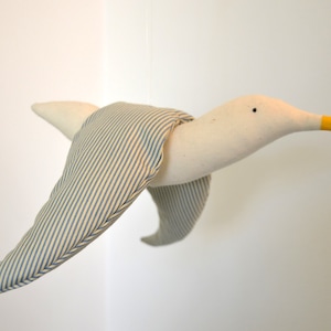 May include: A white fabric seagull with blue and white striped wings and a yellow beak. The seagull is in flight.