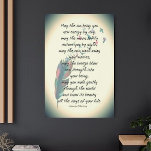 May include: Canvas art print with the text "May the sun bring you new energy by day..." in black script. A colorful feather and small birds accent the text. The artwork is displayed on a dark wall above a wooden cabinet.
