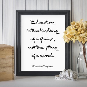 May include: Black framed print with a white background and a quote about education. The quote reads "Education is the kindling of a flame, not the filling of a vessel." The quote is attributed to "Pitanchion Paraphrase".
