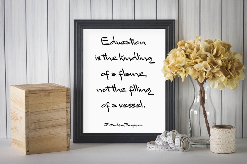 May include: Black framed print with a white background and a quote about education. The quote reads "Education is the kindling of a flame, not the filling of a vessel." The quote is attributed to "Pitanchion Paraphrase".