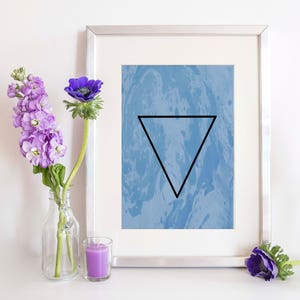 May include: A framed print with a blue and white marbled background and a black triangle in the center. The triangle is an upside-down triangle.