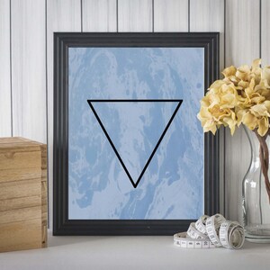 May include: A framed print with a blue and white marbled background and a black triangle in the center. The frame is black and the print is hanging on a white wood wall.