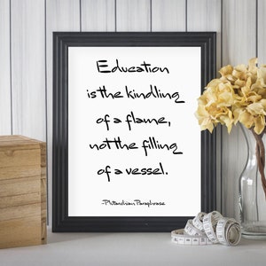 May include: A black framed print with a white background and a quote about education. The quote reads "Education is the kindling of a flame, not the filling of a vessel." The quote is attributed to "Pitanchion Paraphrase".