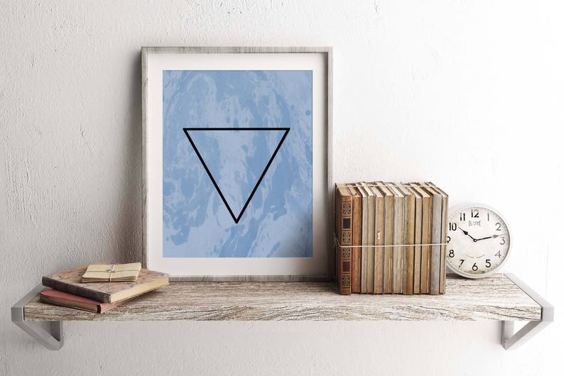 May include: A framed print with a blue and white marbled background and a black triangle in the center. The print is on a wooden shelf with a stack of books and a clock.