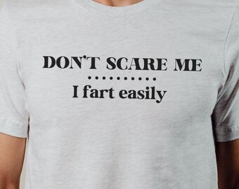 May include: A white t-shirt with the text "DON'T SCARE ME... I fart easily" printed on the front.