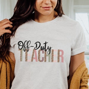 May include: A white t-shirt with the text "Off-Duty Teacher" in black and pink with a leopard print design.