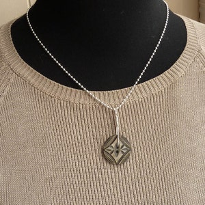May include: A silver ball chain necklace with a silver pendant featuring a black and white geometric design.