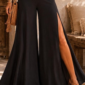 May include: Black wide-leg trousers featuring a high-waisted design and dramatic side slits that extend from the hem to the mid-thigh. The pants are constructed with a flowing, loose silhouette and a solid black color throughout the garment.