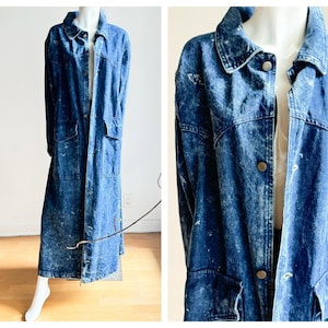 May include: A long, blue denim coat with a button-up front, collar, and two front pockets. The coat has a faded, acid-wash effect and is displayed on a mannequin. The coat's length is visible, extending to the ankles.