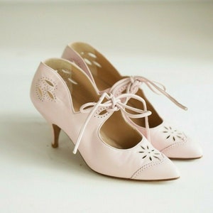 Op de afbeelding: Een paar lichtroze leren hakken met uitsparingen en vetersluiting. De schoenen hebben een spitse neus en een delicate hak.