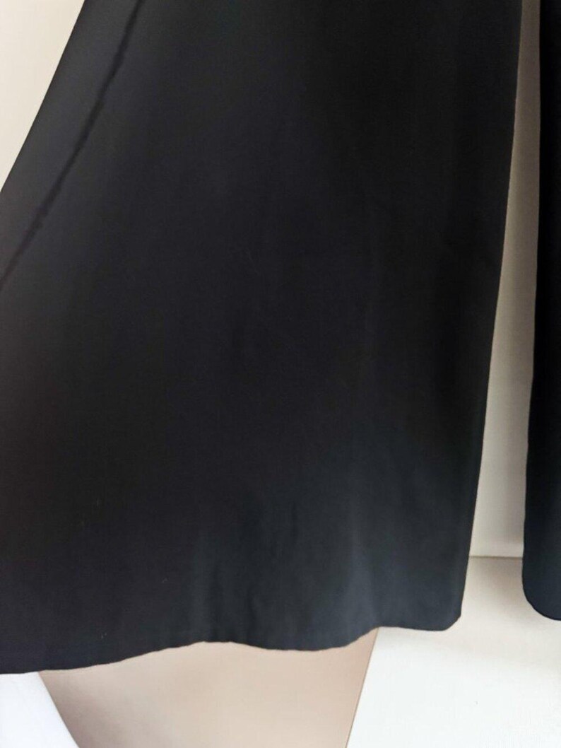 May include: A pair of solid black wide-leg trousers featuring a clean, unadorned design with a straight hemline. The fabric appears smooth and opaque, falling in a relaxed silhouette that extends from the waist down to the lower leg area.