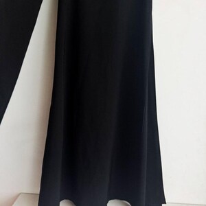 May include: A pair of solid black trousers featuring a wide-leg silhouette. The fabric is opaque and smooth, falling in soft, vertical folds from the waist down to the hem. The design is simple, focusing on the flared cut and the deep black color.