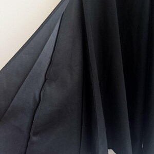 May include: A black skirt featuring a deep side slit that reveals the inner lining of the fabric. The garment is constructed with multiple vertical panels that create a pleated, flowing silhouette, extending downward in a full, flared shape.