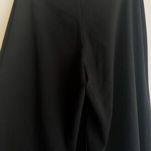 May include: A pair of solid black wide-leg trousers featuring a high-waisted design with a central vertical seam running down the front. The garment is constructed from a smooth, opaque fabric and is suspended from a metal hanger at the top.