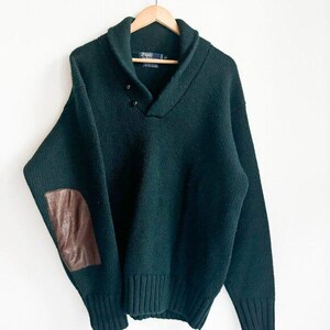 May include: A dark green knitted sweater with a wide collar and a leather patch on the elbow. The sweater has a ribbed hem and cuffs.