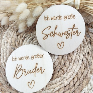 Könnte beinhalten: Zwei Holzschilder mit dem Text "Ich werde großer Bruder" und "Ich werde große Schwester" mit einem Herzsymbol auf jedem.