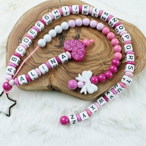 Könnte beinhalten: Eine rosa-weiße Alphabet-Perlenkette mit einem sternförmigen Clip und einem rosa Herz-Anhänger. Die Kette ist mit Perlen besetzt, die den Namen "ALINA" und das Alphabet buchstabieren.