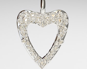 May include: A silver heart-shaped pendant with an intricate filigree design. The pendant has a loop at the top for attaching to a chain.