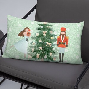 May include: A decorative pillow featuring a watercolor illustration of a ballerina, a nutcracker, and a Christmas tree with ornaments. The background is a light green with a white pattern.