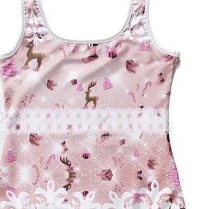Peut inclure: Un maillot de bain une pièce rose et blanc avec un imprimé sur le thème de Noël. L'imprimé représente des rennes, des cannes en sucre, des cadeaux et des flocons de neige. Le maillot de bain est orné d'une bordure en dentelle blanche autour de la taille.