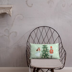 May include: A green and white throw pillow with a Christmas scene featuring a girl in a blue dress, a nutcracker, and a decorated Christmas tree.