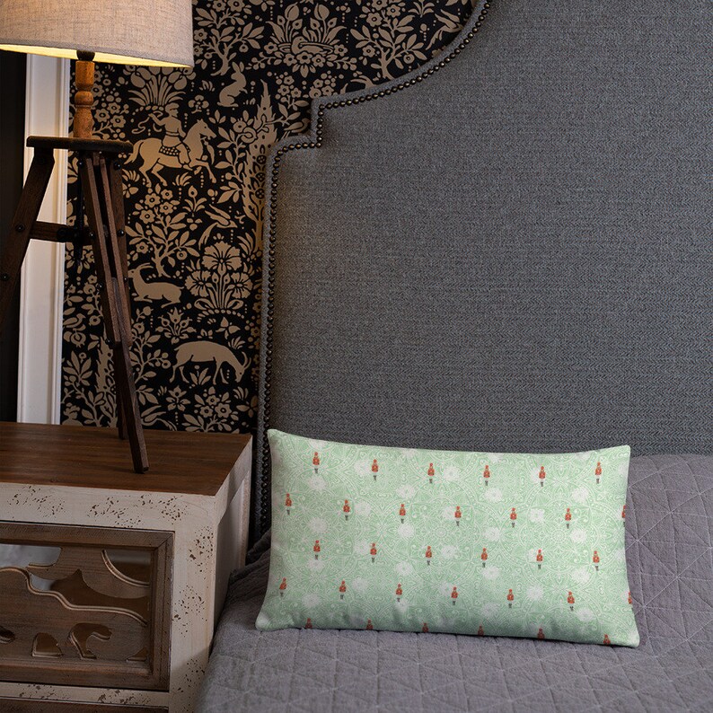 May include: A green and white patterned throw pillow with a repeating design of red and white figures. The pillow is on a gray bed with a gray headboard.