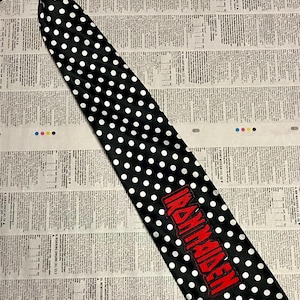 May include: Black tie with white polka dots and the word "IRON MAIDEN" in red. The tie is on a newspaper background. The tie is a classic accessory.