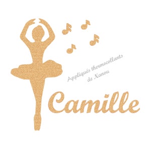 Può includere: Un design dorato glitterato con una ballerina in tutù, note musicali e il nome "Camille" in corsivo. È presente anche il testo "Appliqués thermocollants de Nanou". Il design è su sfondo bianco.