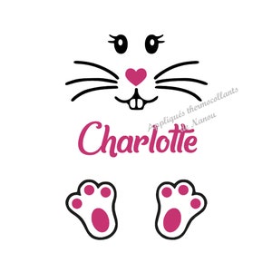 Peut inclure: Graphique blanc représentant un visage de lapin avec des moustaches, des yeux et un nez en forme de cœur noirs. Le nom "Charlotte" est écrit en rose en dessous, avec des pattes de lapin roses en bas.