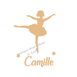 Può includere: Silhouette dorata glitterata di una ballerina in posa aggraziata, con le braccia tese e una gamba distesa. Il nome "Camille" è scritto in glitter dorati sotto, con accenti di stelle. È presente anche il testo "Appliqués thermocollants de Nano".