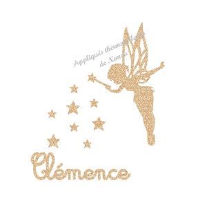 Peut inclure: Une fée dorée scintillante avec un bras tendu et une baguette, entourée d'étoiles. Le nom "Clémence" est écrit en script doré scintillant en dessous des étoiles. Le texte au-dessus de la fée indique "Appliqués thermocollants de Nandu".