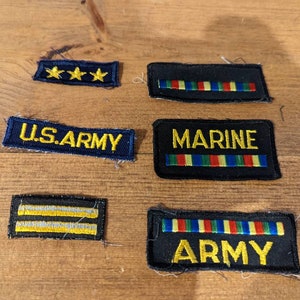 May include: Six embroidered patches with black fabric and yellow thread. The patches include the words "U.S. ARMY", "MARINE", and "ARMY". Two patches have three gold stars. Two patches have a row of colorful stripes.
