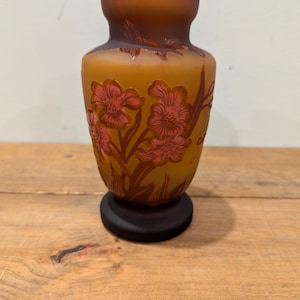 May include: A small, amber-colored glass vase with a floral design. The vase has a brown base and features pink and brown flowers.