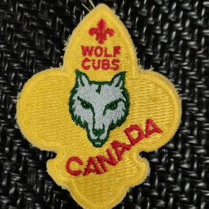 Peut inclure: Écusson brodé jaune avec un logo de louveteau, une fleur de lys et le texte "Wolf Cubs Canada".