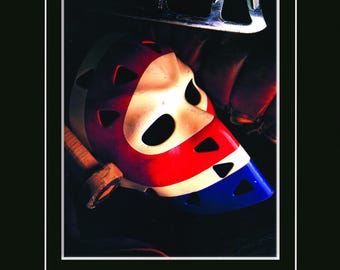 Pode incluir: Imagem emoldurada de uma máscara de goleiro de hóquei vintage, pintada em vermelho, branco e azul. O design da máscara é proeminente, juntamente com um patim de hóquei. A imagem inclui o texto "KEN DRYDEN Montreal Canadiens 1971-1979".