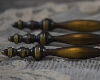 May include: Four antique brass drawer pulls with ornate details. The pulls are arranged in a row on a white lace fabric background.