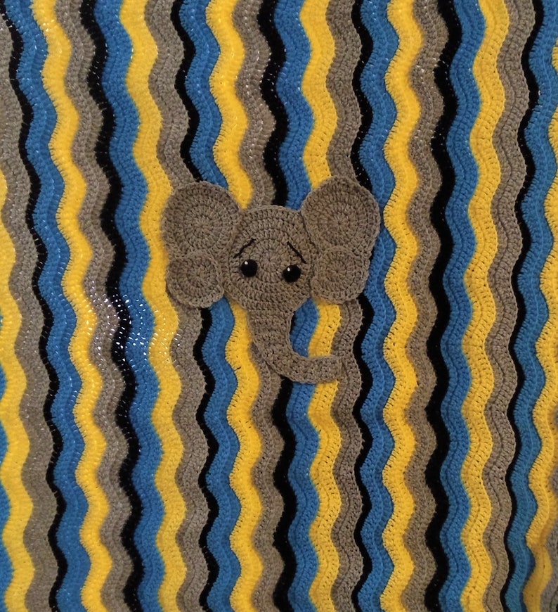 May include: A crocheted baby blanket featuring a grey elephant applique. The blanket is made with yellow, blue, grey, and black yarn in a wavy pattern.