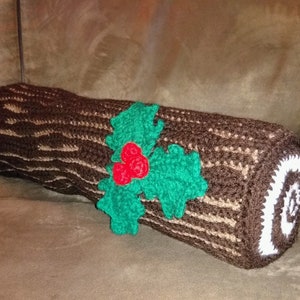 May include: A brown and white crocheted log pillow with a green and red holly design.
