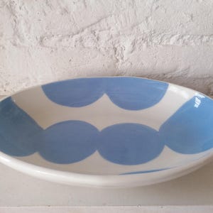 May include: A white oval ceramic serving bowl with a blue and white geometric pattern. The bowl has a slightly irregular shape and a glossy finish.