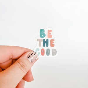 May include: A white sticker with the words "BE THE GOOD" in colorful, stylized letters. The letters are in shades of blue, green, pink, and gray.